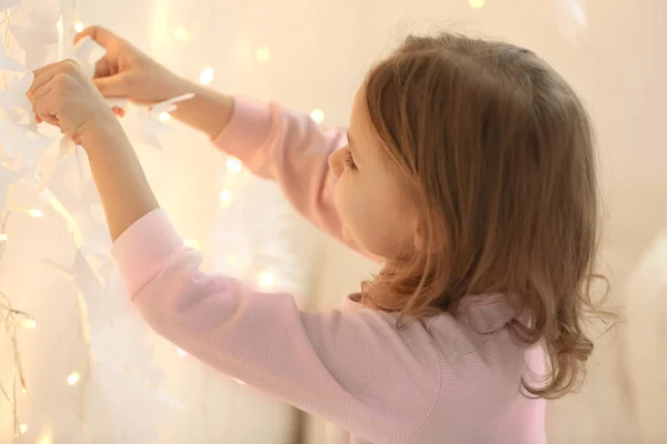 Милая маленькая девочка украшает комнату с гирляндой и бумажными снежинками — стоковое фото