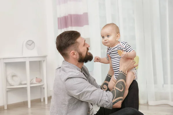 Handsome tattooed young man playing with cute little baby at home — Stock Photo, Image