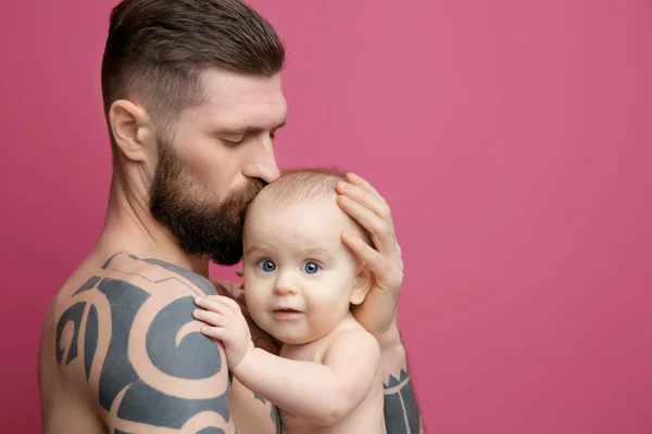 Beau jeune homme tatoué tenant mignon petit bébé sur fond de couleur — Photo