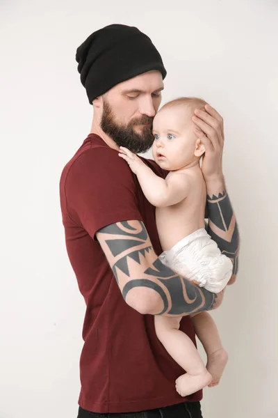 Beau jeune homme tatoué tenant mignon petit bébé sur fond clair — Photo