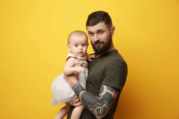 Beau jeune homme tatoué tenant mignonne petite fille sur fond de couleur — Photo