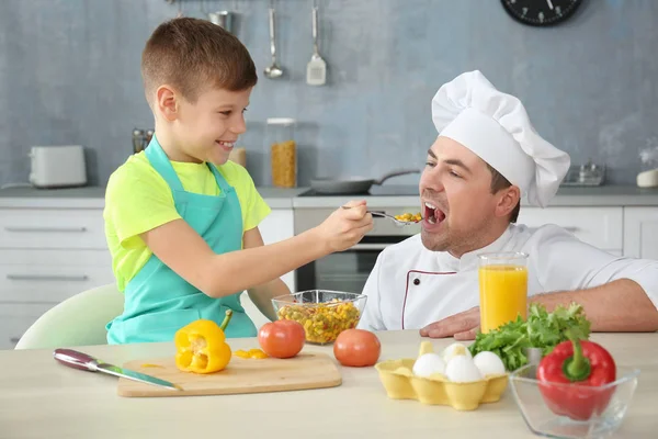 Malý chlapec krmení otce v kuchyni při vaření dohromady — Stock fotografie
