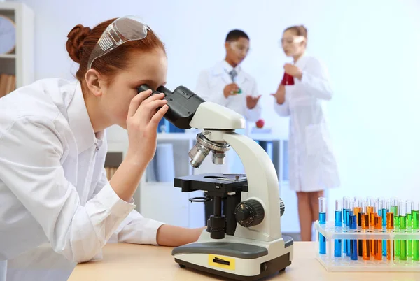 Hermosa chica de la escuela mirando a través del microscopio en clase de química — Foto de Stock