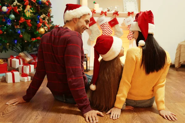 Family sitting near fireplace in living room decorated for Christmas
