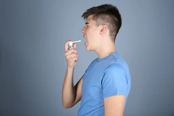 Sick young man using throat spray on color background — Stock Photo, Image