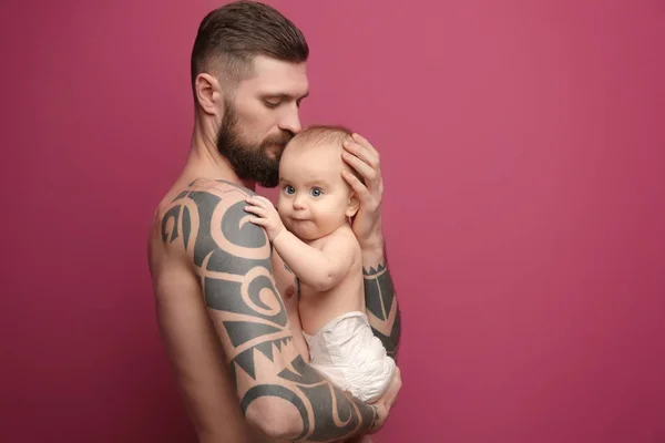 Guapo tatuado joven sosteniendo lindo bebé en color de fondo — Foto de Stock