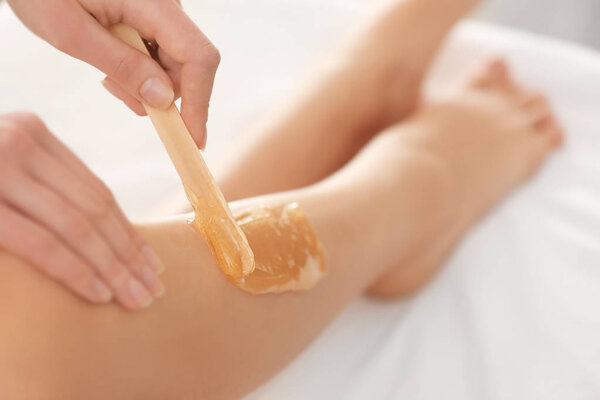 Beautician waxing female legs 