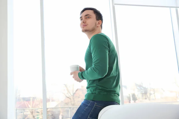 Happy young man with cup of coffee resting at home — Stock Photo, Image