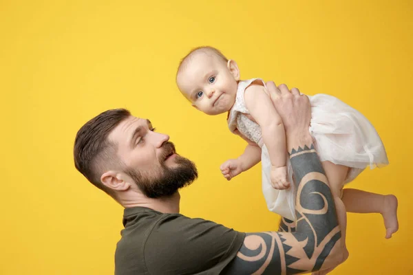 Bello tatuato giovane uomo holding carino bambina su colore sfondo — Foto Stock