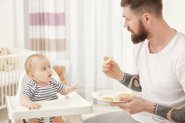 Handsome tattooed young man feeding cute little baby at home — Stock Photo, Image