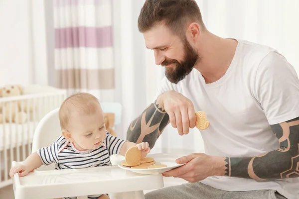 Guapo tatuado joven alimentación lindo bebé en casa — Foto de Stock