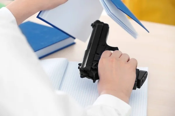 Schoolboy sitting at desk with gun — Stock Photo, Image