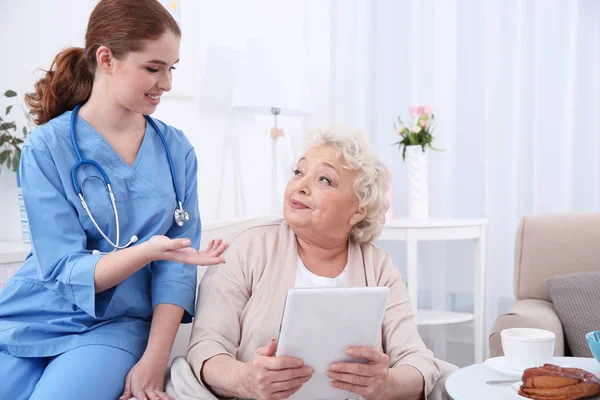 Verpleegkundige helpen oudere vrouw om te werken op tablet pc op lichte kamer — Stockfoto