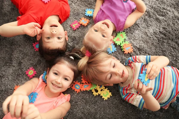 Crianças pequenas bonitos brincando com figuras coloridas enquanto deitado no tapete em casa — Fotografia de Stock