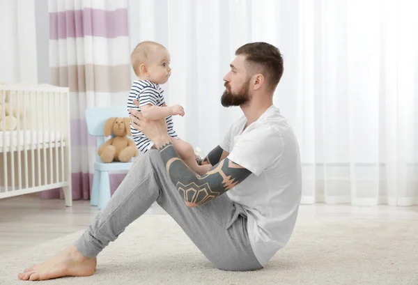 Bonito jovem tatuado brincando com o bebê em casa — Fotografia de Stock