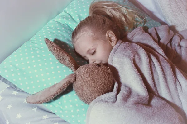 Söt tjej med leksak kanin sover i sängen — Stockfoto