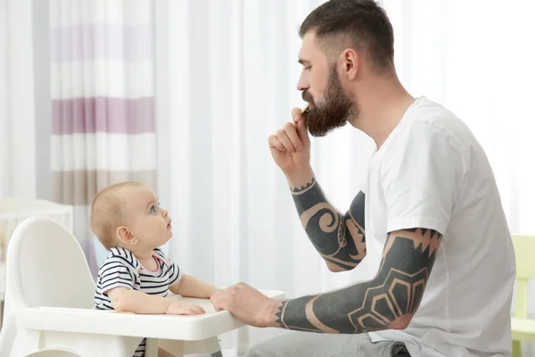 Bonito tatuado jovem homem alimentando bonito pequeno bebê em casa — Fotografia de Stock