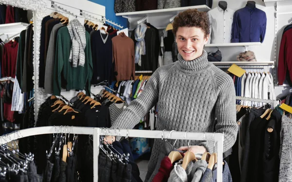 Bello giovane uomo che sceglie i vestiti nel negozio moderno — Foto Stock