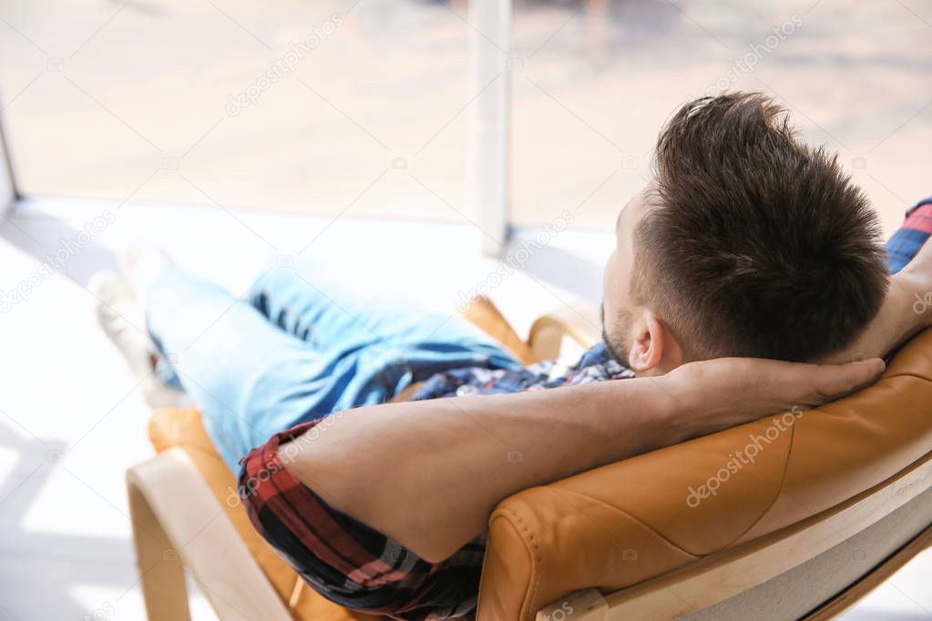 Happy young man resting in armchair 