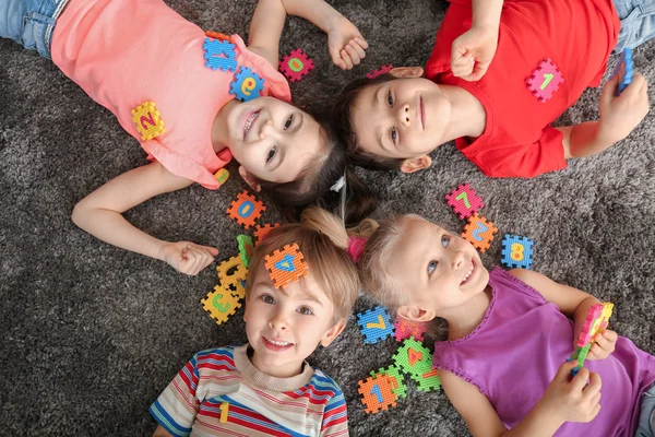 Милые маленькие дети играют с красочными фигурами, лежа дома на ковре — стоковое фото