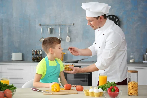Pai alimentando filho na cozinha enquanto cozinhando juntos — Fotografia de Stock