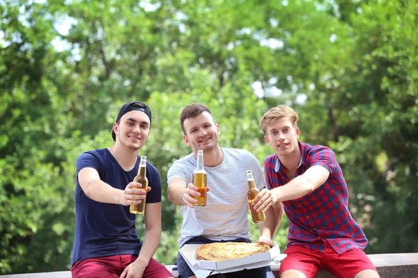 Drie mannelijke vrienden met pizza en bier op bomen achtergrond — Stockfoto