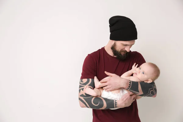 Beau jeune homme tatoué tenant mignon petit bébé sur fond clair — Photo