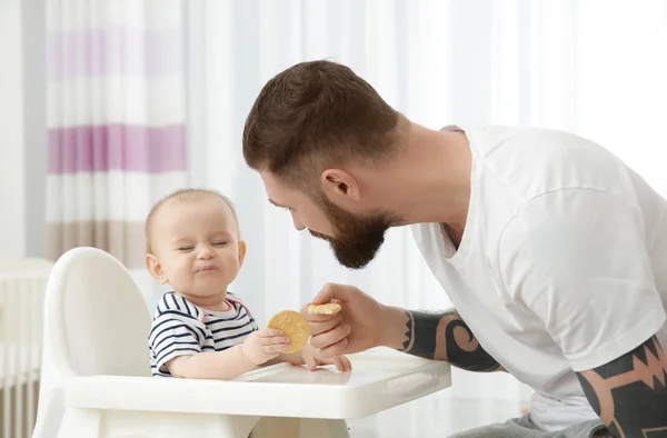 Bonito tatuado jovem homem alimentando bonito pequeno bebê em casa — Fotografia de Stock