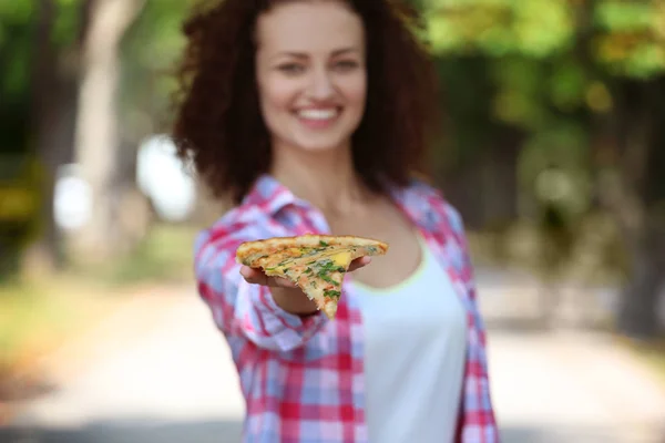 Young beautiful woman with slice of pizza on blurred natural background — Stock Photo, Image