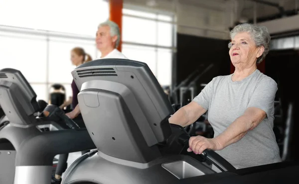 Senior vrouw draait op loopband in de sportschool — Stockfoto