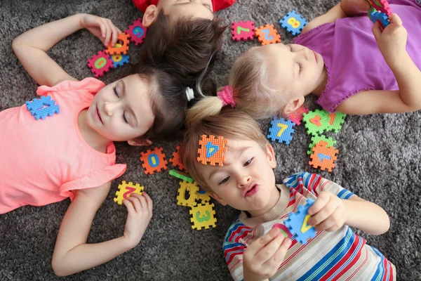 Милые маленькие дети играют с красочными фигурами, лежа дома на ковре — стоковое фото