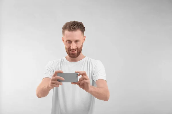 Schöner Mann beim Fotografieren mit dem Handy, auf hellem Hintergrund — Stockfoto