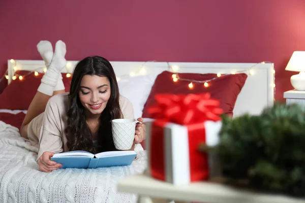 Vacker ung kvinna läsa bok liggande på sängen hemma — Stockfoto