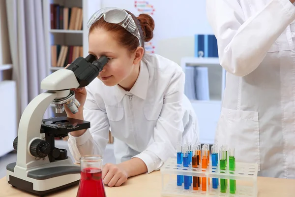 Hermosa chica de la escuela mirando a través del microscopio en clase de química — Foto de Stock