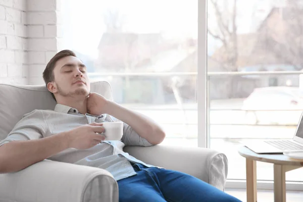 Joven feliz con taza de café descansando en sillón —  Fotos de Stock