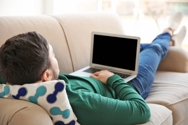 Happy young man lying on sofa with laptop — Stock Photo, Image