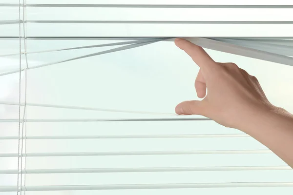 Vrouwelijke hand scheiden van de latten van de blinds te doorzien venster — Stockfoto