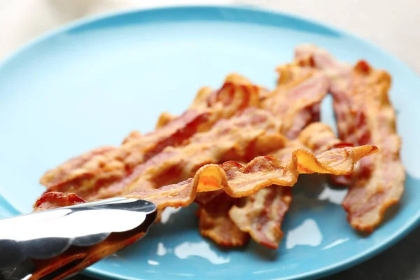 Tenant une savoureuse tranche de bacon avec pinces — Photo