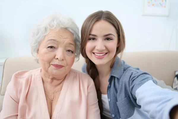 Beautiful girl with grandmother taking selfie on couch at home — Stock Photo, Image