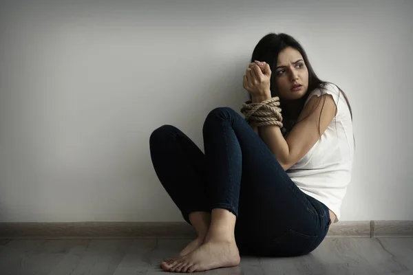 Vrouw met gebonden handen zittend op de vloer tegen lichte muur — Stockfoto