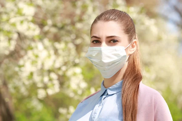 Chica joven con mascarilla entre los árboles en flor en el parque —  Fotos de Stock