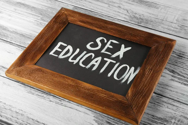 Небольшая доска с текстом SEX EDUCATION на деревянном столе — стоковое фото