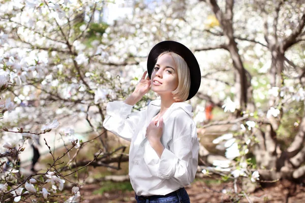Młoda dziewczyna w kapeluszu w pobliżu kwitnące drzewo — Zdjęcie stockowe
