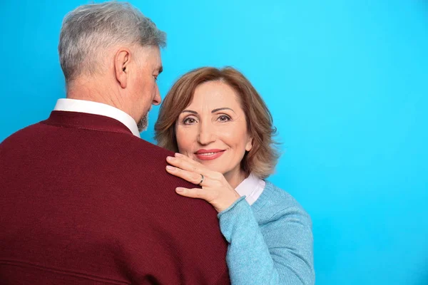 Mulher sênior feliz abraçando seu marido no fundo de cor — Fotografia de Stock
