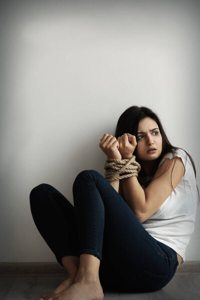 Woman with tied hands sitting on floor against light wall