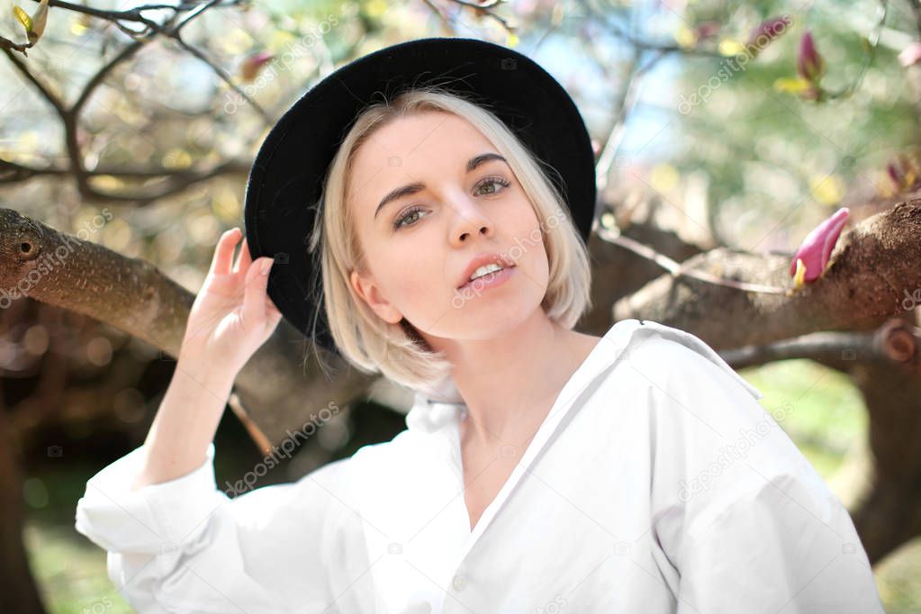 Young woman in hat near magnolia tree 