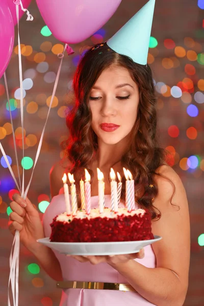 Όμορφη νεαρή γυναίκα με τούρτα γενεθλίων και μπαλόνια εναντίον defocused φώτα — Φωτογραφία Αρχείου