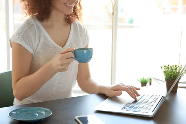 Schöne junge Frau mit einer Tasse Kaffee am Tisch sitzend und mit Laptop — Stockfoto