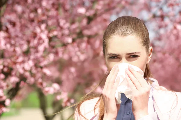 Niña estornuda con limpiaparabrisas entre árboles florecientes en el parque —  Fotos de Stock