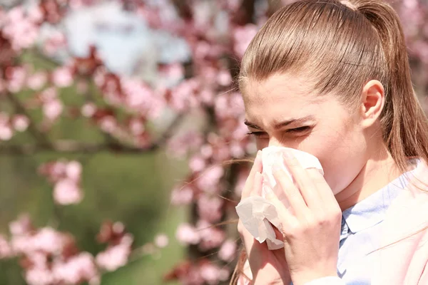 Kýchací mladá dívka s hladící nos mezi kvetoucí stromy v parku — Stock fotografie
